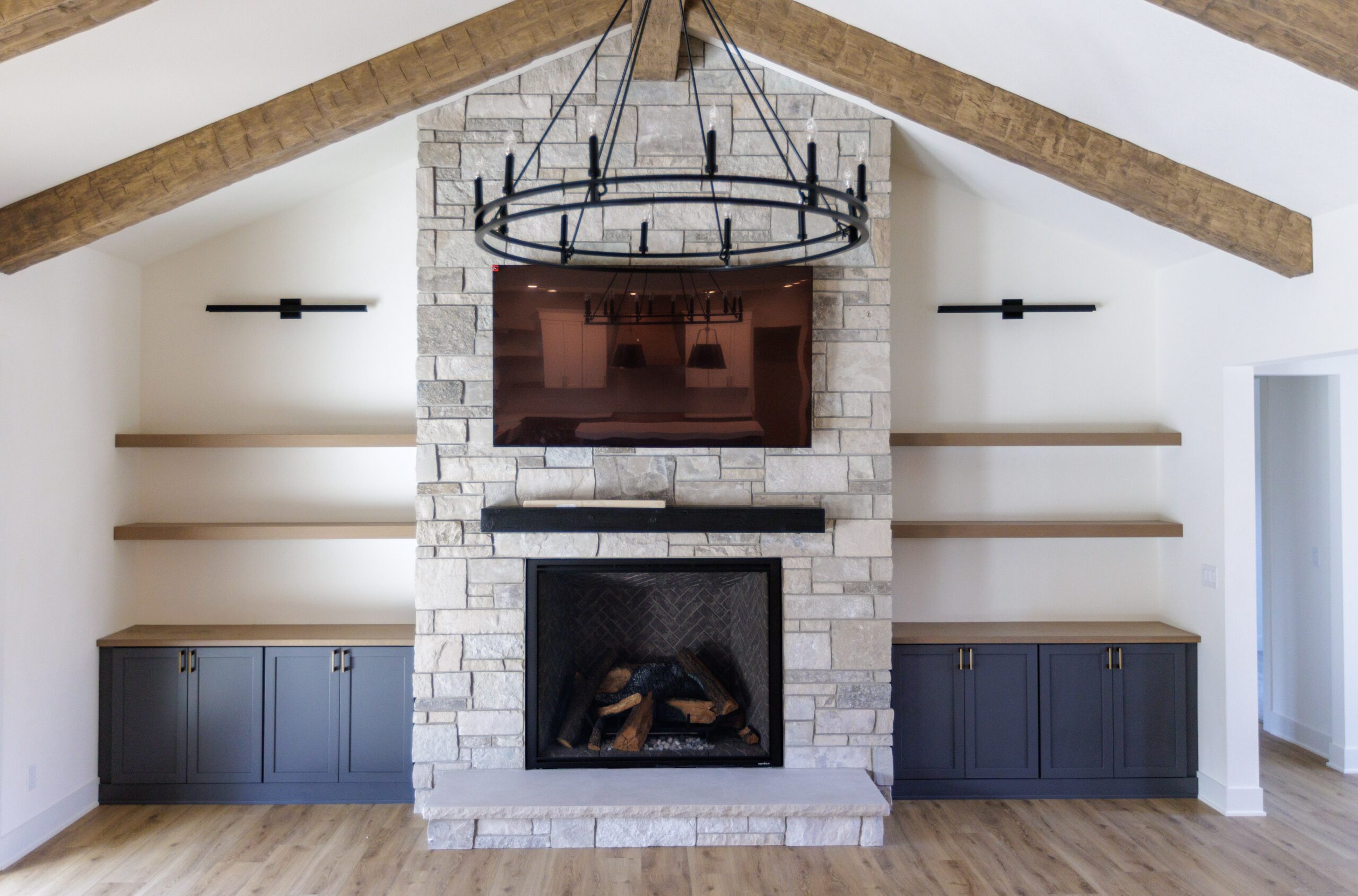 Living room in Merton home with stone fireplace, exposed wood beams, built-in cabinets, and chandelier