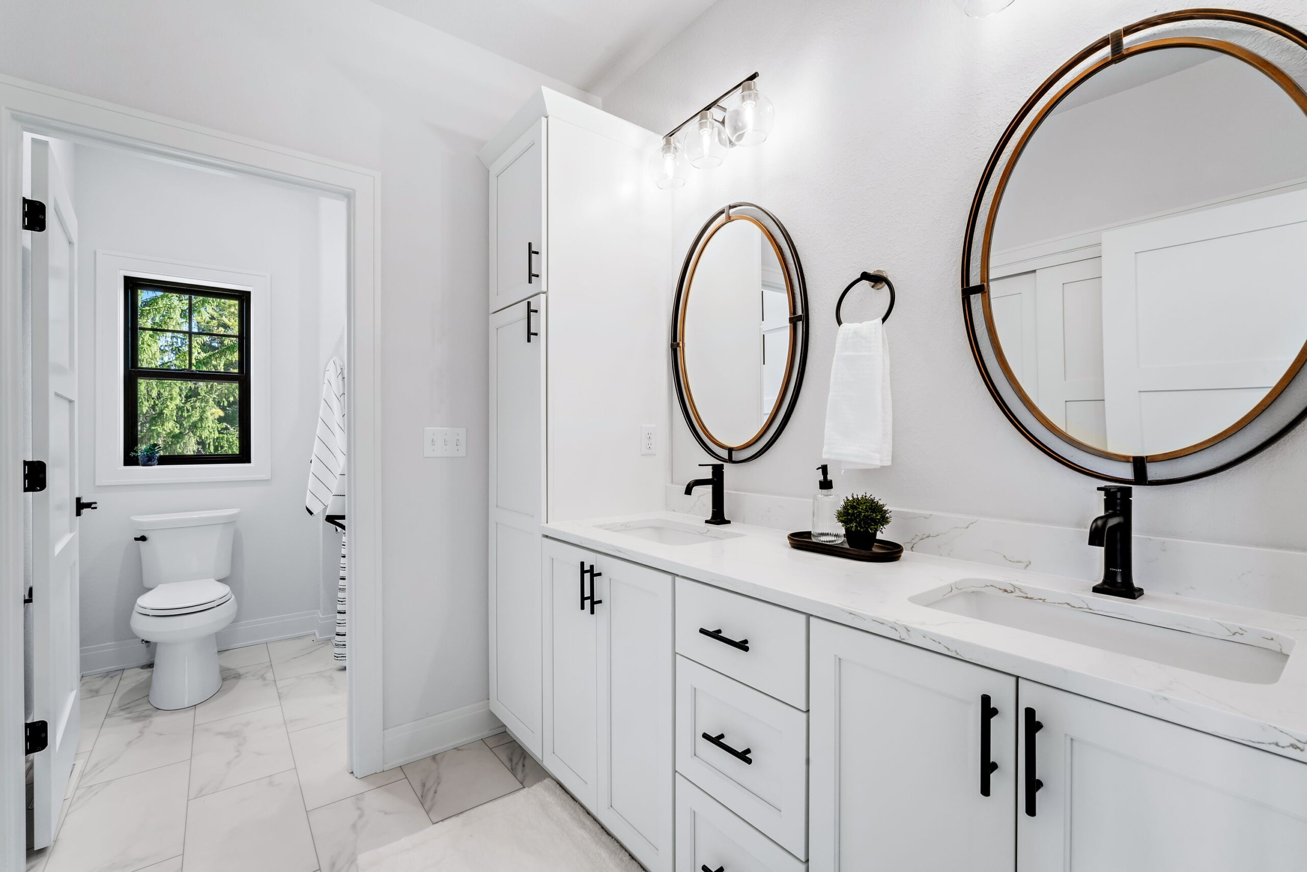Bathroom with double vanity, round mirrors, black fixtures, and white cabinetry
