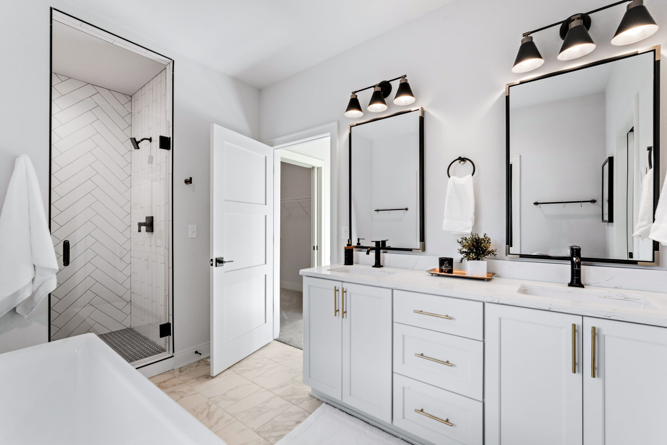 Bathroom with walk-in tile shower, double vanity, black fixtures, white cabinets, and modern lighting