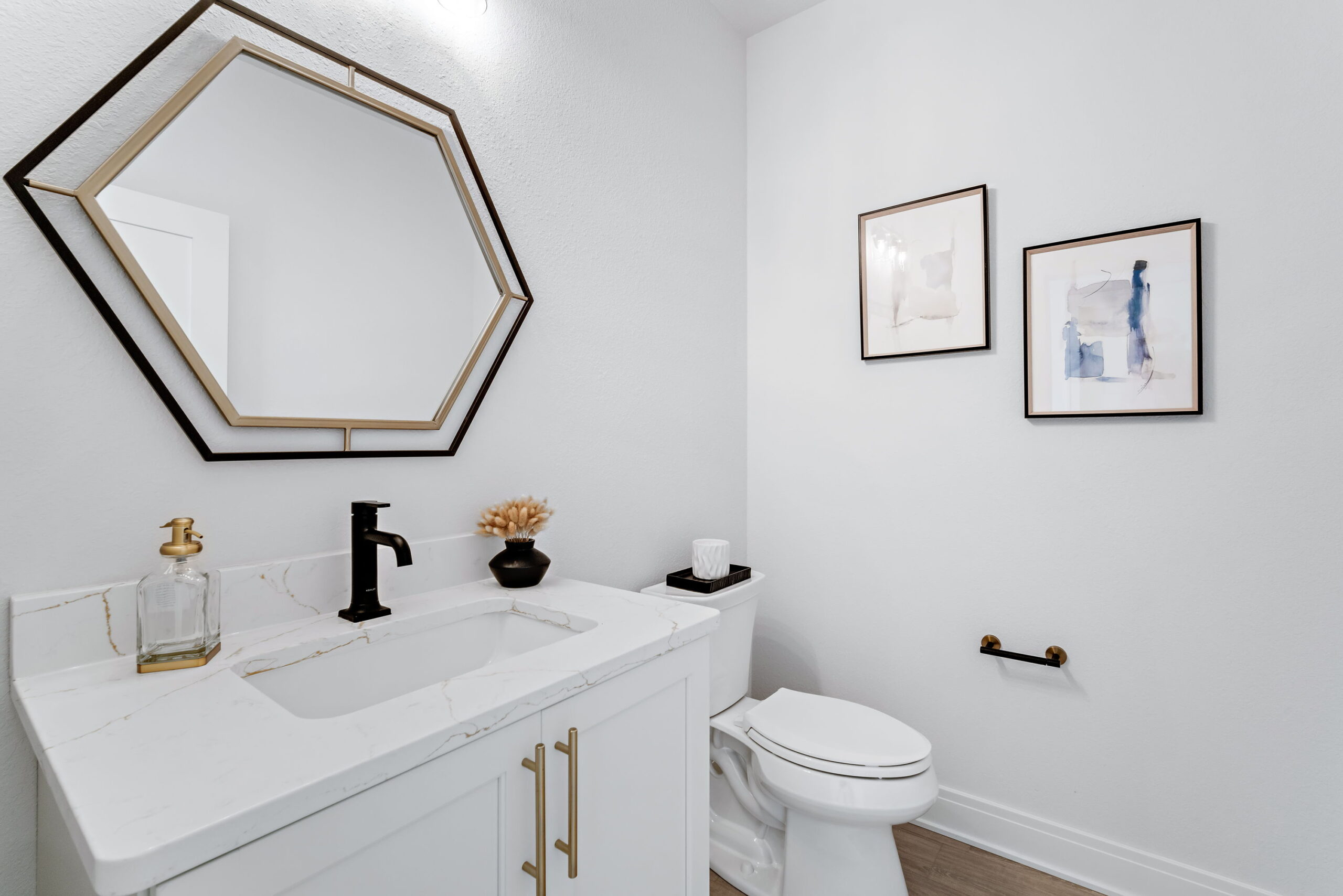 Powder room with modern vanity, geometric mirror, black faucet, and decorative wall art