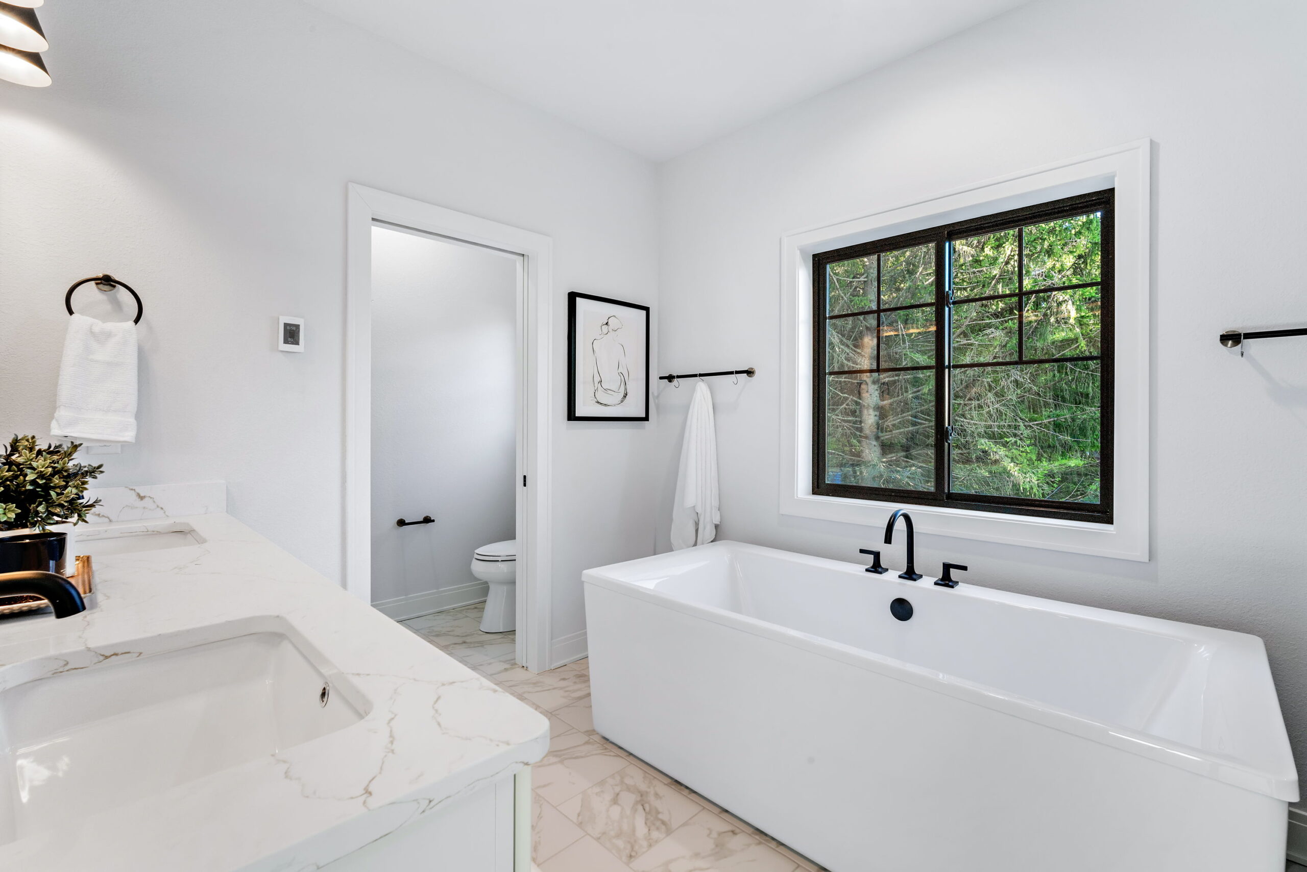 Bathroom with freestanding soaking tub, large window, white cabinets and granite countertop with black fixtures