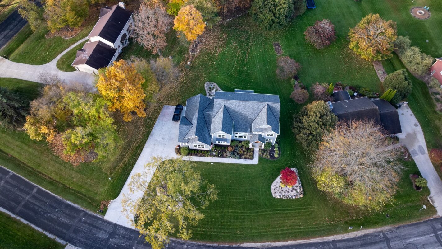top down aerial view of custom home with landscaped yard, driveway, and surrounding trees