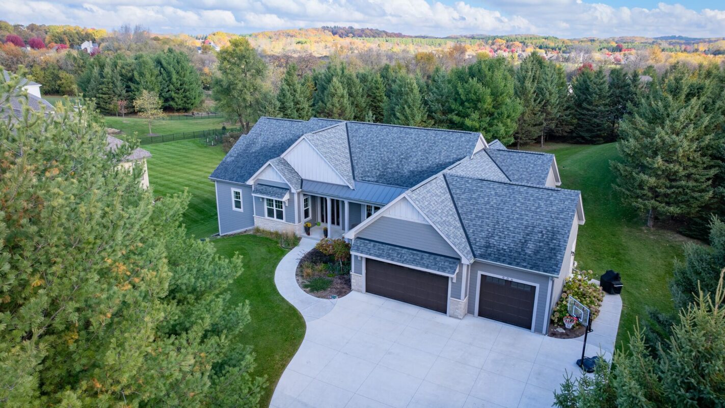aerial view of custom home with three car garage, gray siding, and curved driveway