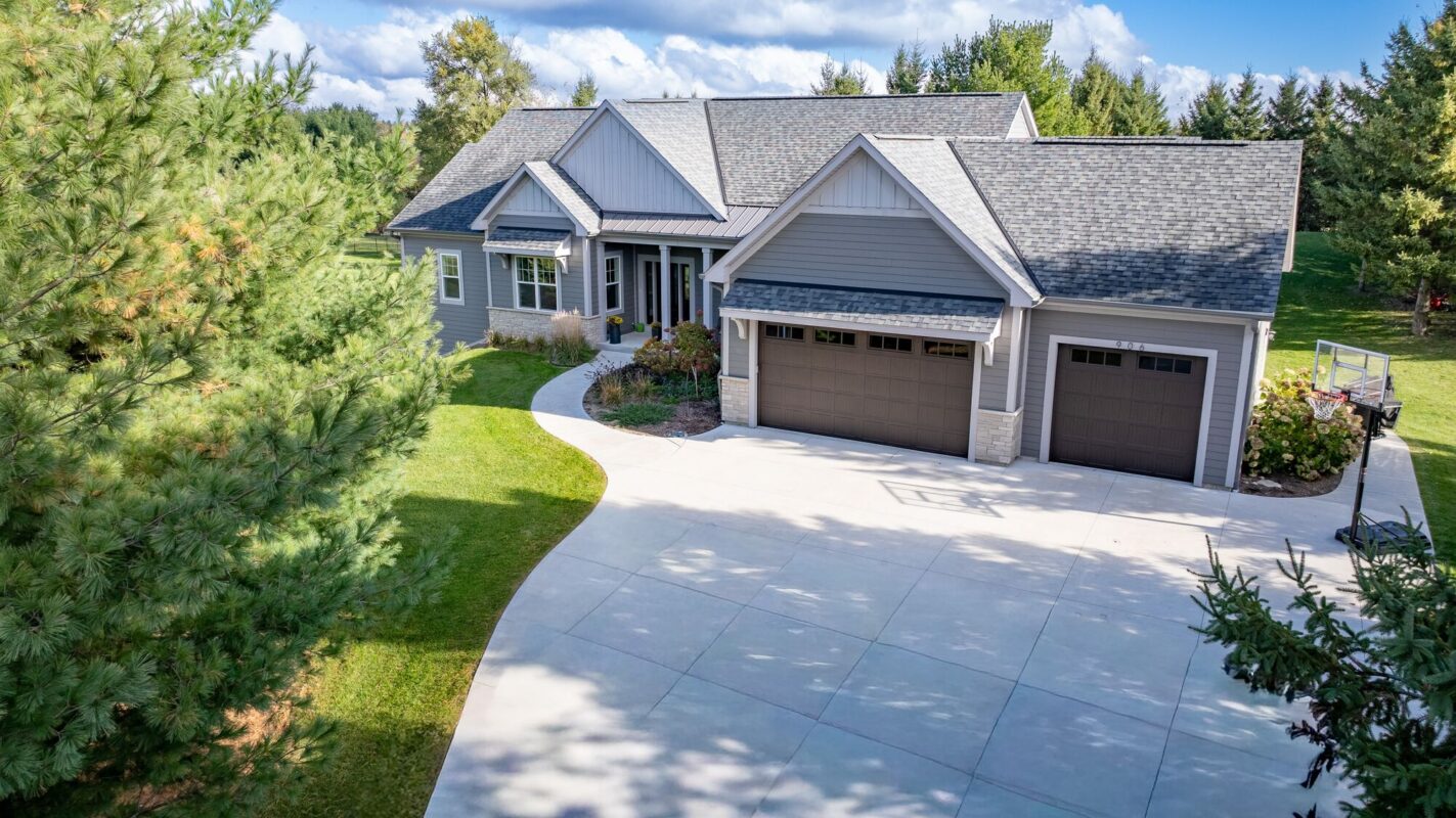 custom home exterior with gray siding, curved driveway, and three car garage