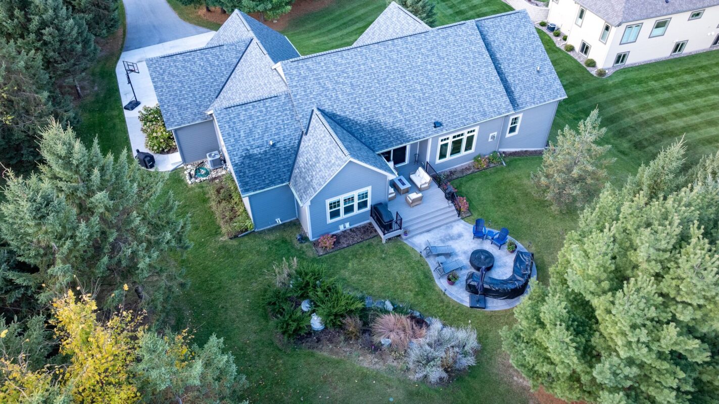aerial view of custom home backyard with patio seating area, landscaping, and surrounding trees