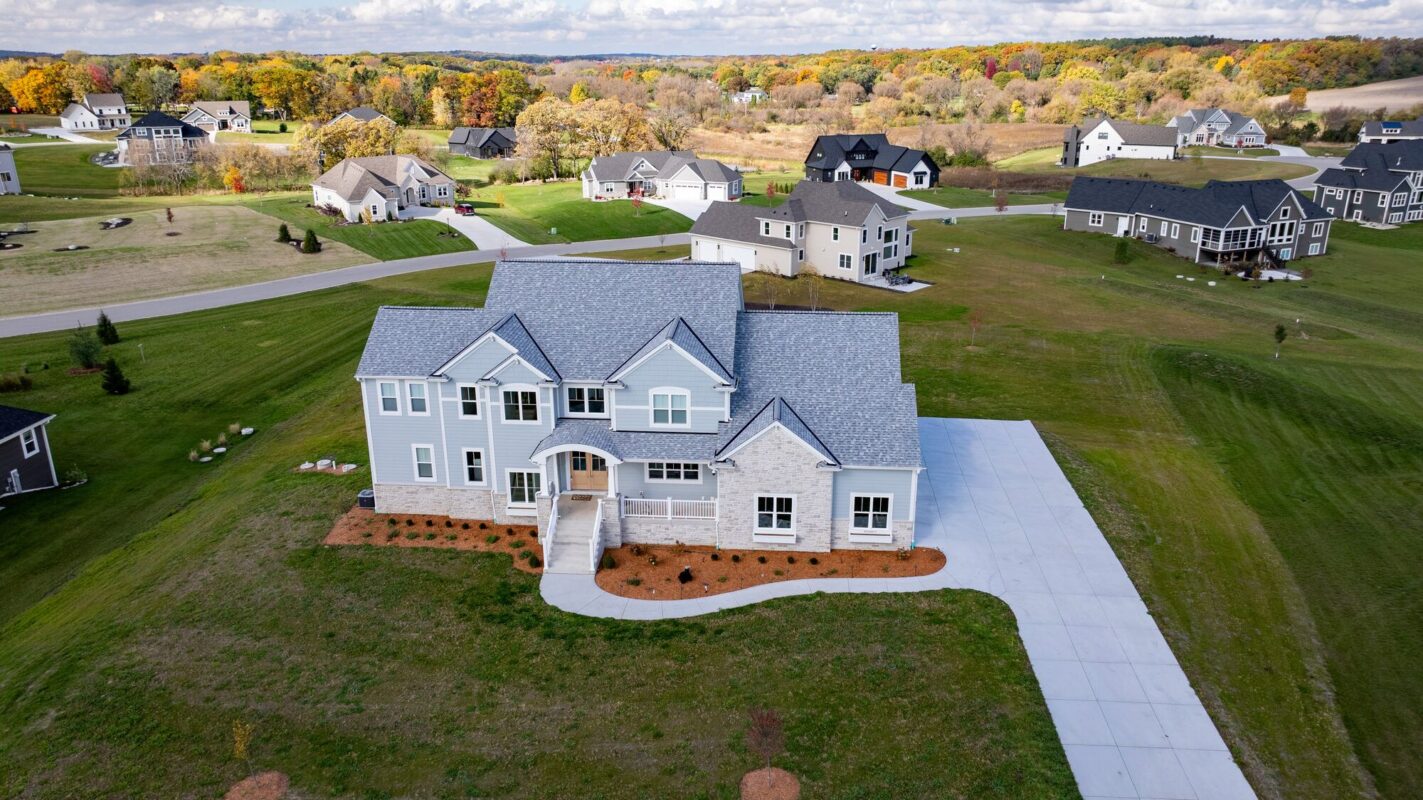 aerial view of custom home front elevation with long driveway and open lot in residential neighborhood
