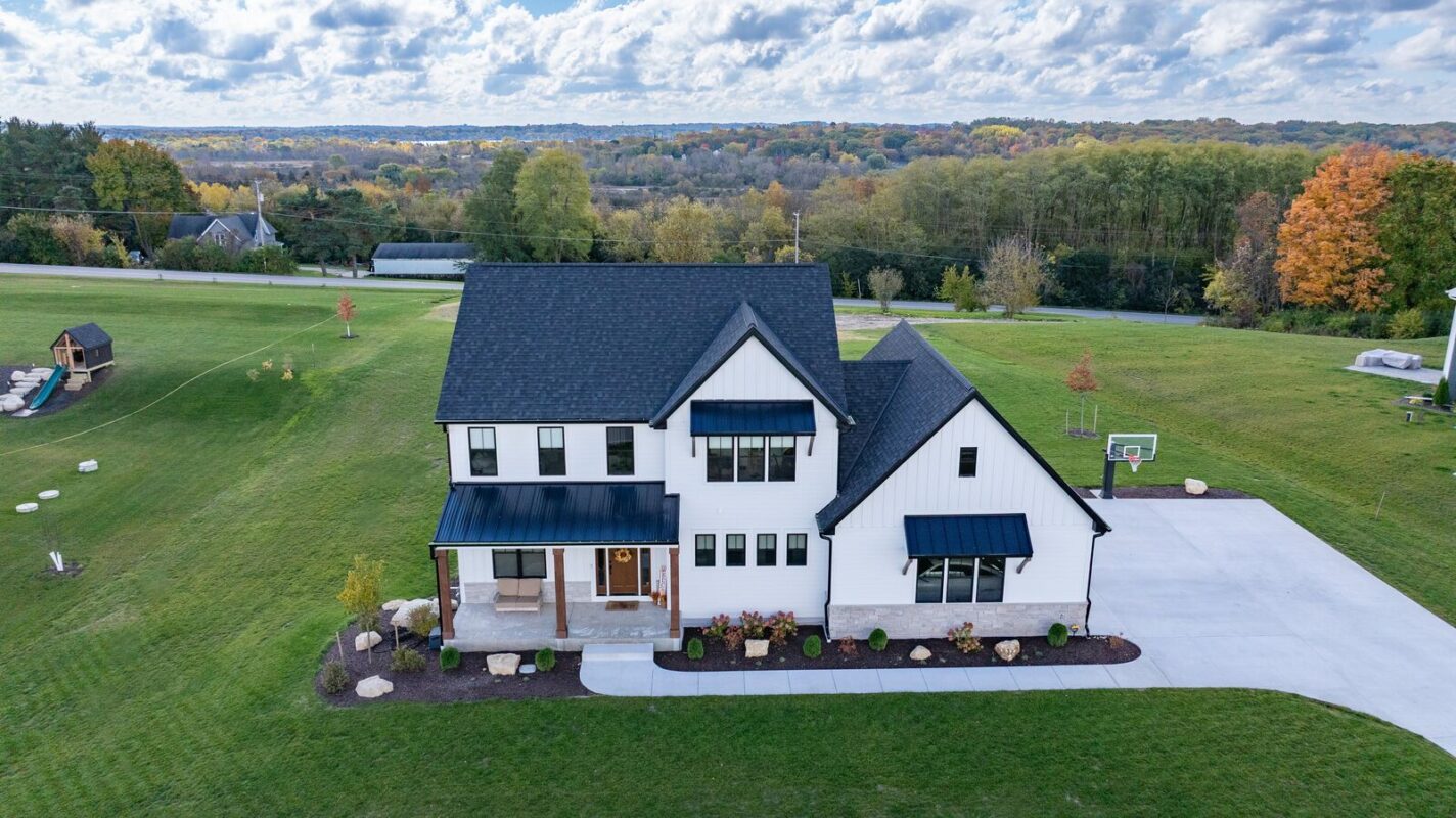 aerial view of custom modern farmhouse with white exterior, black roof, and large driveway