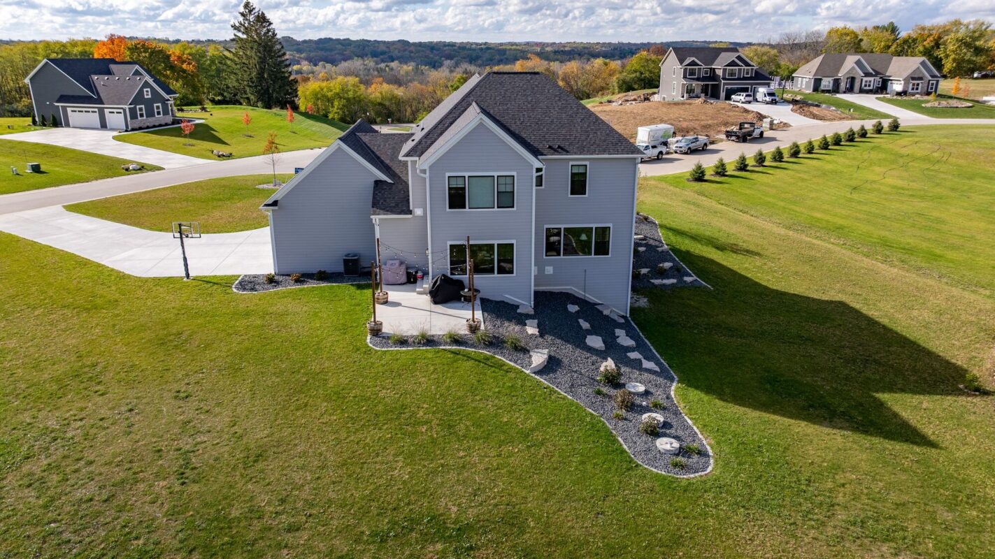 aerial view of custom home backyard with patio, landscaped yard, and open green space