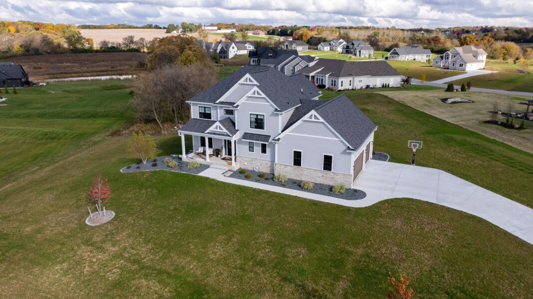 aerial view of custom home with front porch, curved driveway, and large open yard