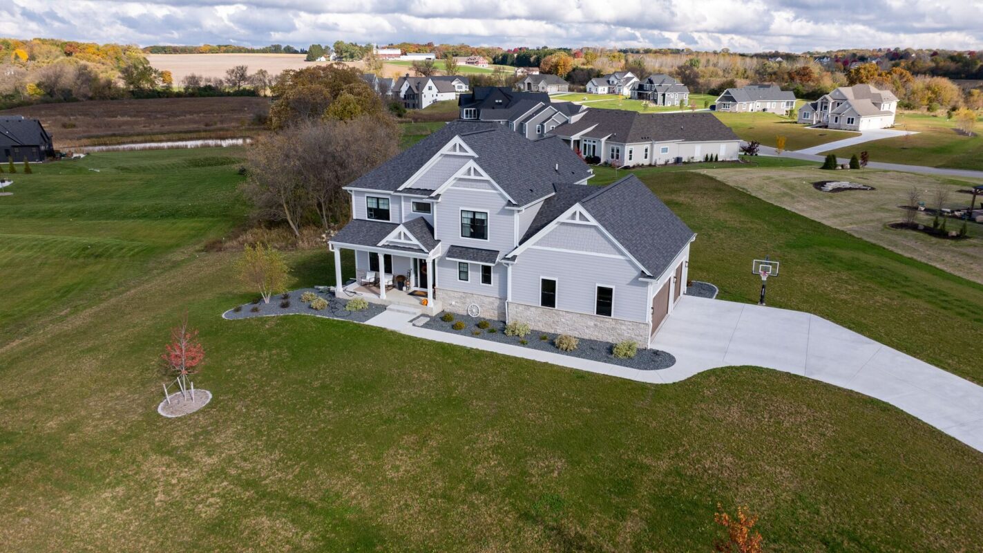 aerial view of custom home with front porch, curved driveway, and large open yard