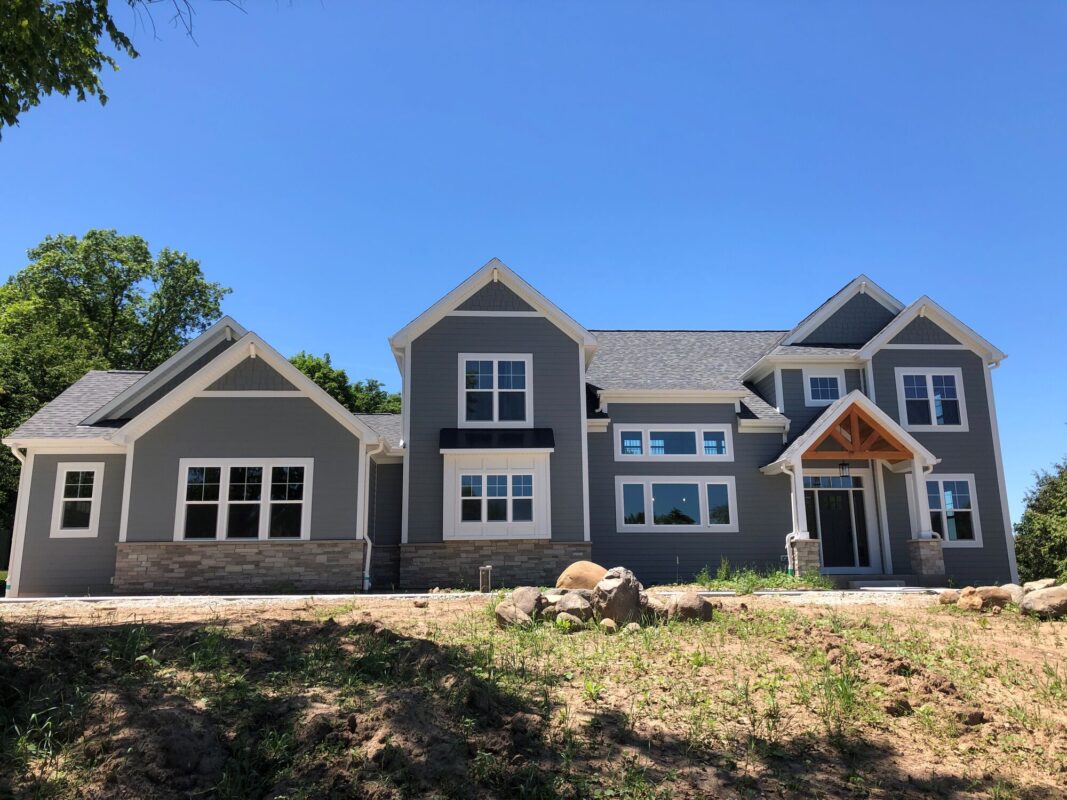 custom home exterior with gray siding, gabled rooflines, and covered front entry