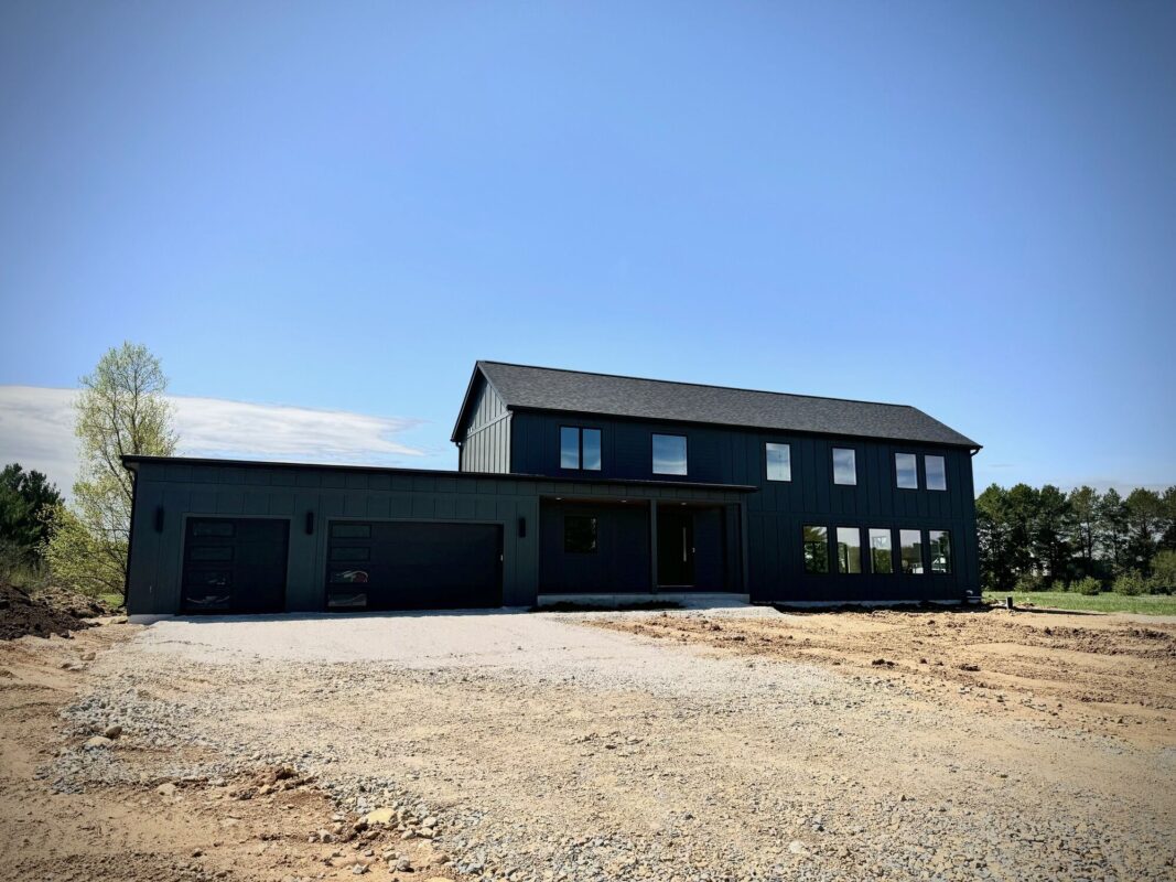 modern custom home exterior with dark siding, attached garage, and large windows on a spacious lot