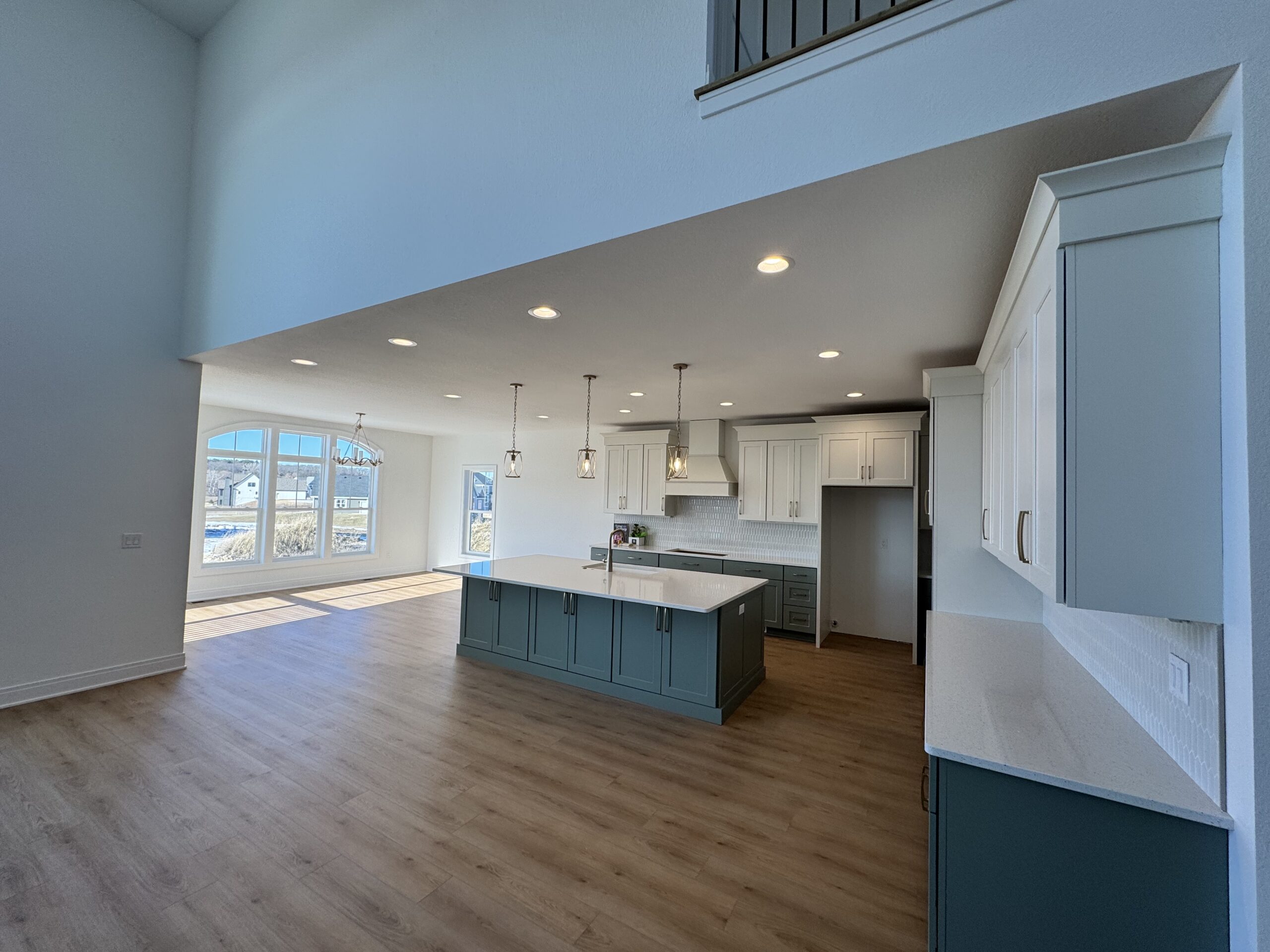 Morrow Home open concept kitchen with large island, white upper cabinets and sage green lower cabinets, and spacious living area