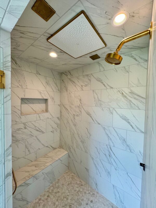 custom home walk-in shower with marble tile, rainfall showerhead, and built-in bench