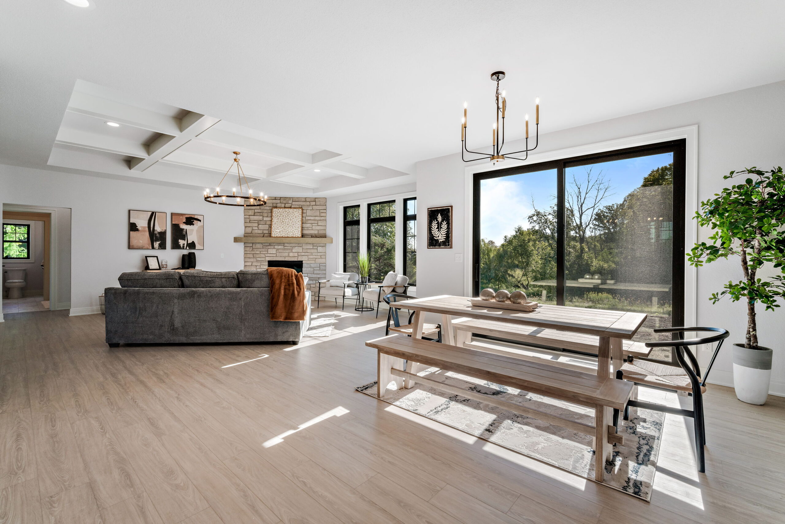 Open concept living and dining area with stone fireplace, coffered ceiling, and large sliding glass doors overlooking backyard