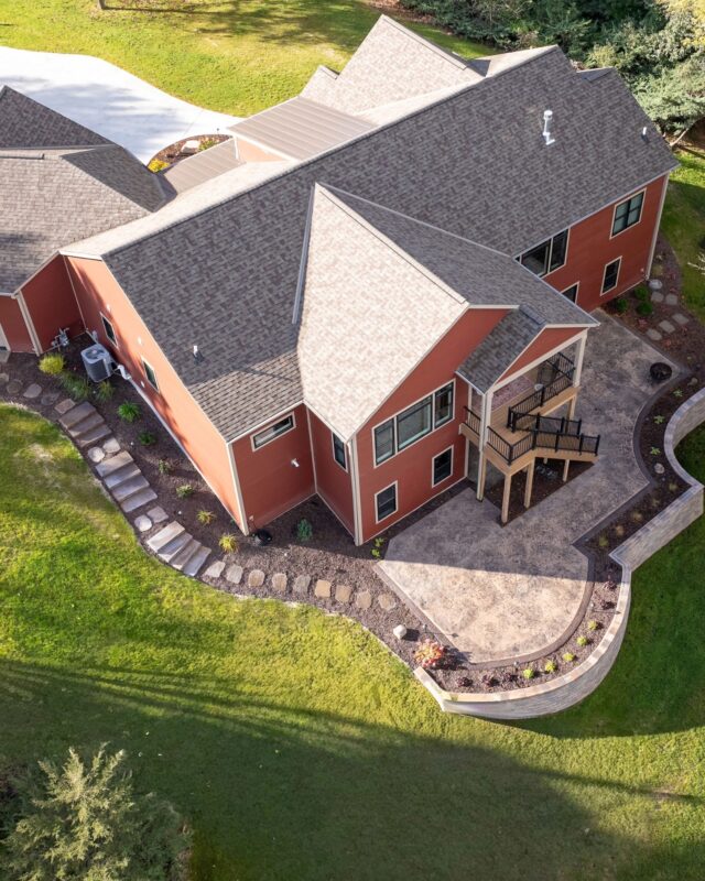 custom home aerial view of backyard with elevated deck, patio, retaining wall, and landscaping