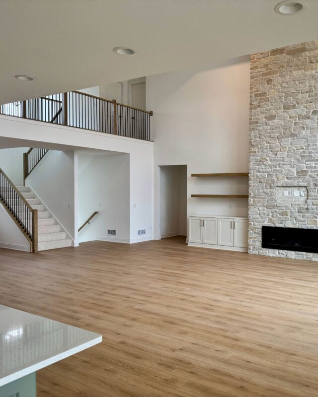 Morrow Home living room with tall ceilings, stone fireplace, and open loft staircase